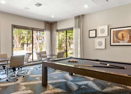 A pool table is in the middle of a room with a view of trees outside the window.