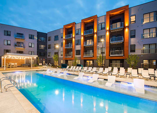 2 Bedroom Luxury Apartments in Berkley Riverfront, MO - Union Berkley - Resort-Style Pool with Spacious Sundeck, Submerged and Poolside Lounge Chairs, and View of Apartment Buildings.
