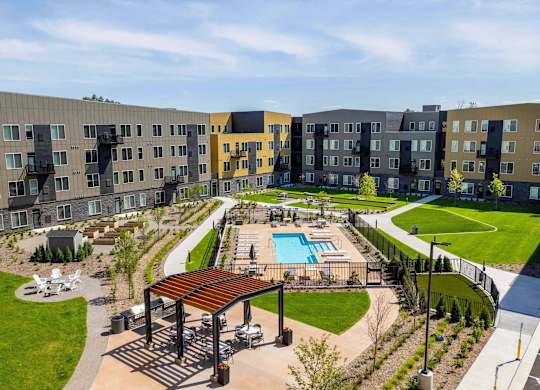 A large outdoor swimming pool is surrounded by a grassy area and a wooden pavilion.