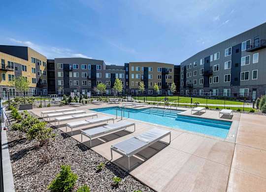 A large swimming pool surrounded by sun loungers and apartment buildings.