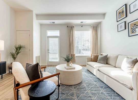 A living room with a white couch, a wooden chair, and a small table with a vase on it.