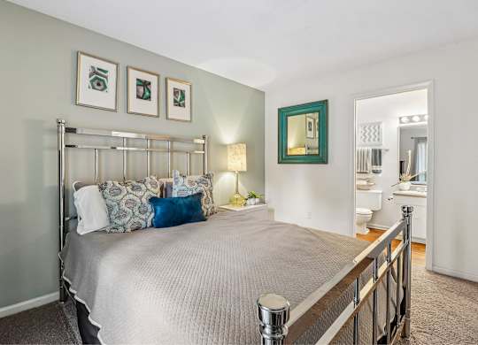 A bedroom with a bed, pillows, a mirror, and a nightstand.