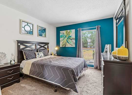 A bedroom with a bed, nightstand, and a window with blinds.