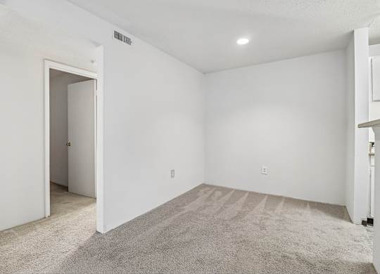 A white room with a carpeted floor and a doorway leading to another room.
