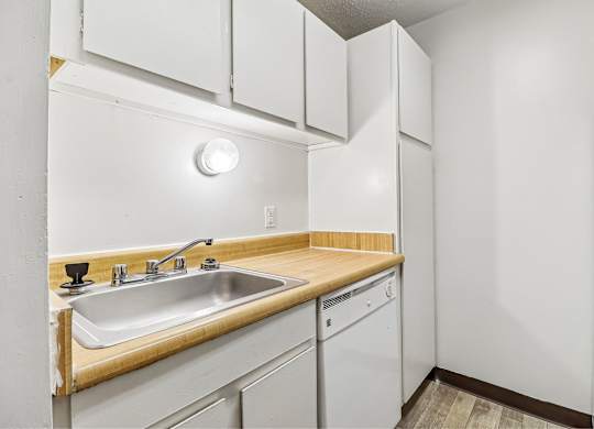 A kitchen with a white fridge, sink and cabinets.