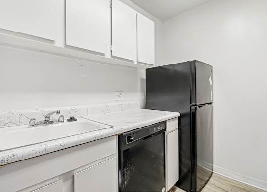 A black refrigerator is in a kitchen with white cabinets.