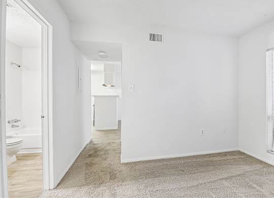 A white room with a carpet on the floor and a window on the right side.