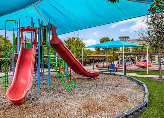 A playground with a red slide and a blue canopy at Twin Creeks Crossing