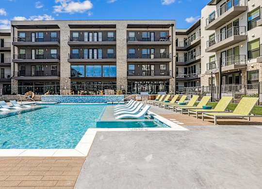 A large swimming pool surrounded by lounge chairs and buildings.