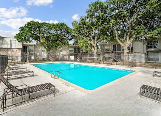 A swimming pool surrounded by trees and lounge chairs in a residential area.