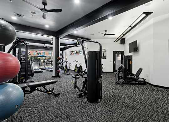 A gym with a variety of equipment including a weight machine, a bench, and a fan.