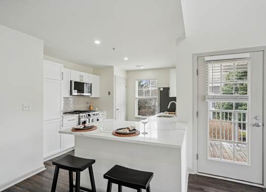 A kitchen with white cabinets and a white island with a counter top and two black stools.