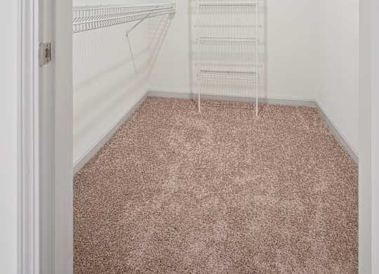 A walk-in closet with white shelving and a pink carpet.