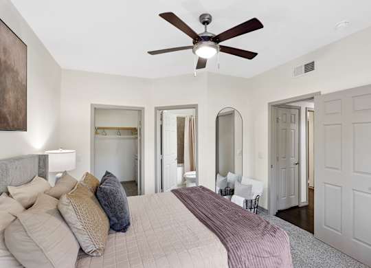 A bedroom with a bed, a ceiling fan, and a mirror.