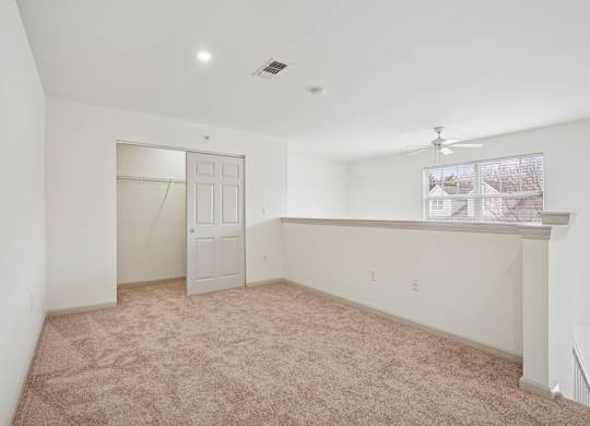 A room with a carpeted floor and a ceiling fan.