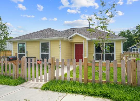A yellow house with a red door and a wooden fence.