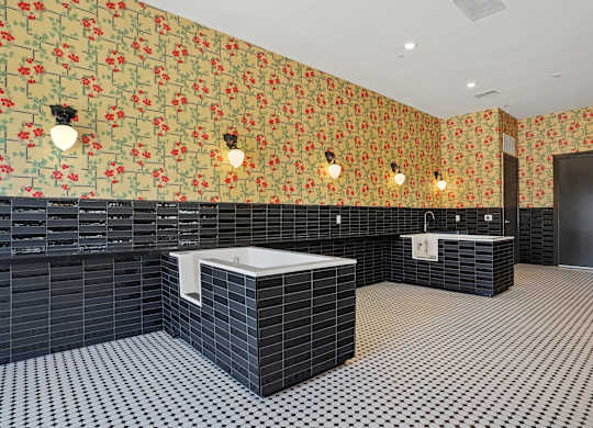 A bathroom with a black and white checkered floor, a black tiled wall, and a floral wallpaper.