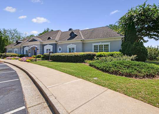 A house with a grey roof and white trim is surrounded by green bushes and trees.