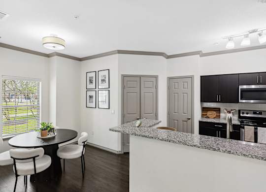 A kitchen with a table and chairs in the foreground and a countertop with a plant on it.