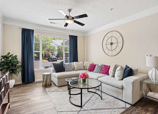 A living room with a white couch, a glass table, and a ceiling fan.