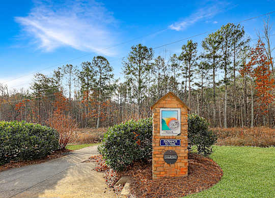 A sign in front of a road with a blue sky and trees in the background.