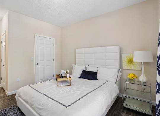 A bedroom with a white bed and a nightstand with a lamp.