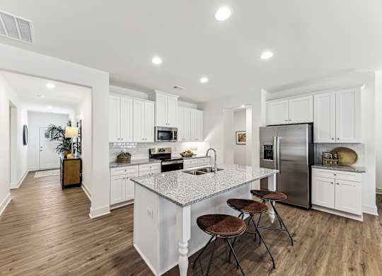 a white kitchen with a marble counter top and a stainless steel refrigerator