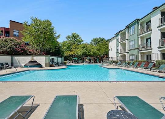 A large swimming pool surrounded by lounge chairs and trees.