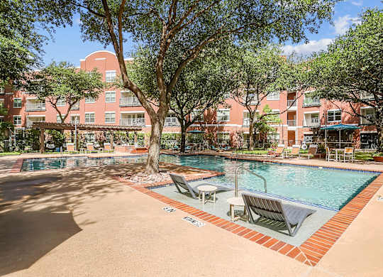 A pool surrounded by trees and chairs in front of a red building.