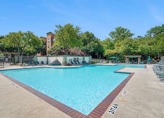 A large swimming pool surrounded by trees and a building in the background.