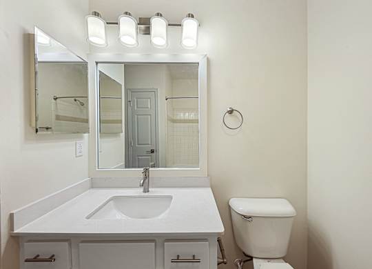 A white bathroom with a sink, toilet, and mirror.