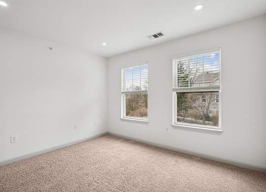 A large empty room with carpeted floor and two windows.