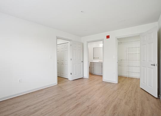 A room with white walls and wooden flooring, with a door on the left and a closet on the right.