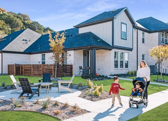 a mother pushing her child in a stroller on a backyard patio with a house
