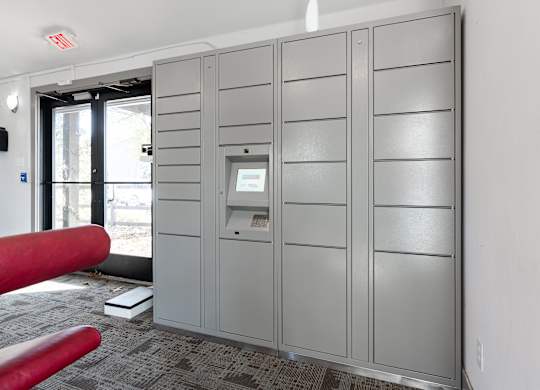 A grey metal locker room with a red bench and a door with a window.