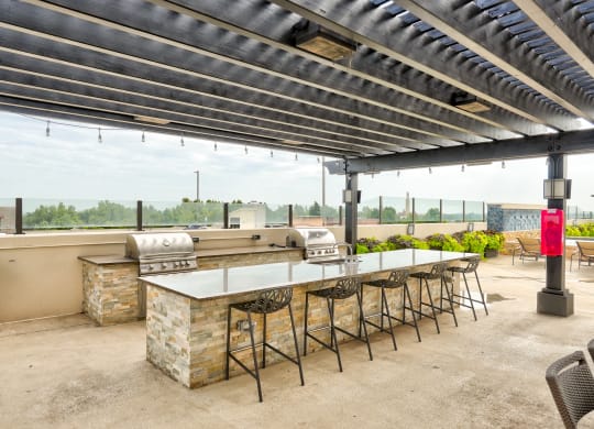 an outdoor patio with a barbecue grill and a long table with stools