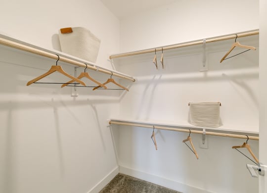 a walk in closet with white walls and wooden hangers