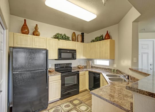 Modern kitchen here at Natura Villas Apartments with light wood cabinets, black appliances, and marble countertops. Decorative vases and greenery adorn the upper cabinets for a cozy touch.