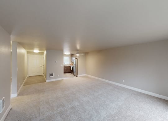 an empty living room with a kitchen in the background