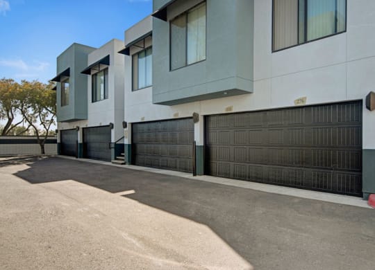 Modern townhouse exterior here at Acclaim Apartments featuring three garage doors with black paneling, large windows above, set against a clear blue sky, creating a clean, contemporary look.
