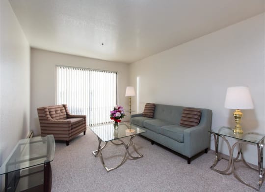 A modern living room here at Outlook Apartments with a gray sofa, striped armchair, glass coffee table, and two glass side tables with lamps. A vase with flowers adds color.