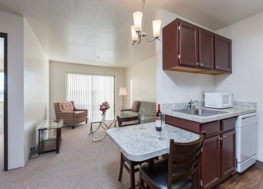 Cozy living area here at Outlook Apartments with striped armchairs, glass table, and flowers. Kitchenette has marble countertops and wine. Bright, relaxed ambiance.
