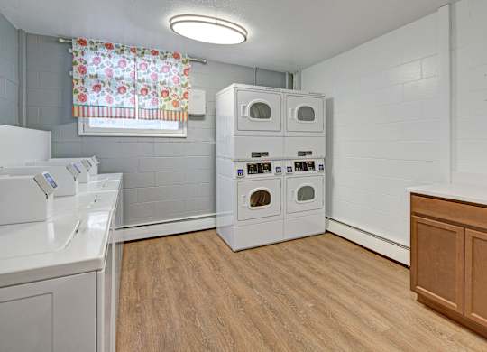 A laundry room with a washer and dryer, a window with a floral curtain, and a wooden cabinet.