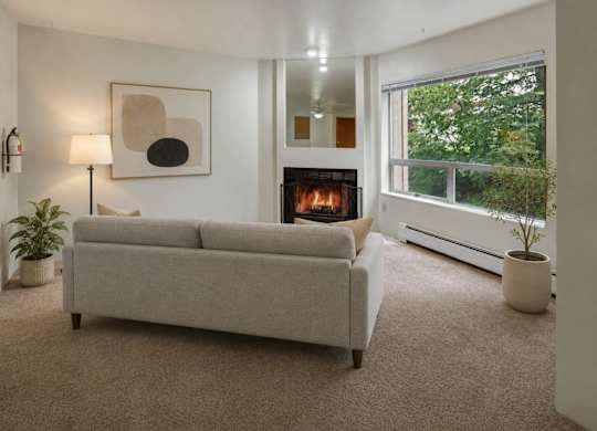 A living room with a grey couch, a fireplace, and a painting on the wall.