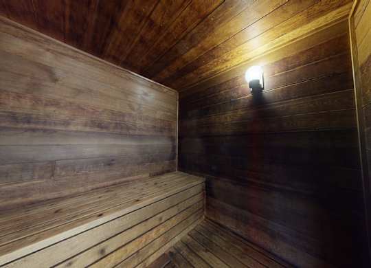 A warm, cedar-lined sauna here at Club at Eagle Pointe featuring wraparound wooden bench seating, rich wood-paneled walls and ceiling, and soft wall-mounted lighting that creates a relaxing, spa-like atmosphere ideal for unwinding, relieving stress, and enjoying quiet moments after a workout.
