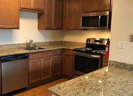 A spacious kitchen here at Club at Eagle Pointe featuring warm wood cabinetry, granite-style countertops, and stainless steel appliances including a refrigerator, range, microwave, and dishwasher. The functional L-shaped layout offers generous counter space, ample storage, and a breakfast bar ideal for meal prep and casual dining.