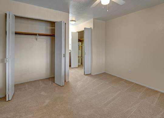 A spacious bedroom here at Club at Eagle Pointe showcasing soft neutral carpeting, light-toned walls, and an open layout with generous floor space. The room features a large closet with bi-fold doors and ample hanging storage, plus a ceiling fan and overhead lighting that enhance comfort and everyday functionality.