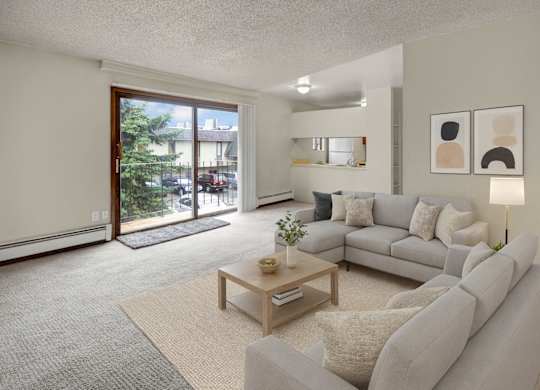 A bright living room here at Deer Park featuring a spacious open layout with a light gray sectional sofa, neutral throw pillows, a wooden coffee table, and soft area rug, complemented by modern wall art, a floor lamp, and sliding glass doors that open to a private balcony with outdoor views.