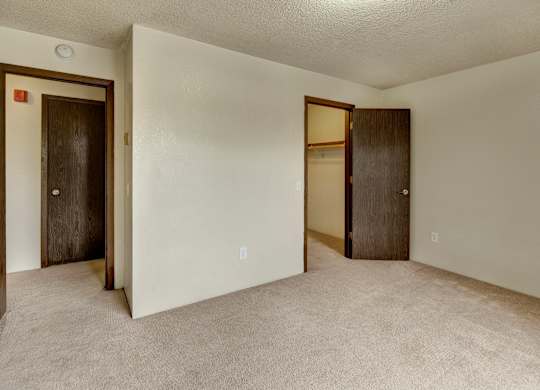 Spacious bedroom here at Deer Park showcasing soft carpet flooring, light neutral walls, and a clean, open layout. The room features a walk-in closet with shelving, a separate entry door, and ample wall space for flexible furniture placement, creating a comfortable and functional sleeping area.