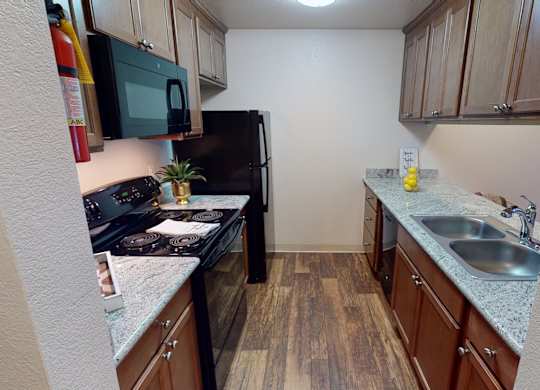 A compact kitchen here at Hillside Chalet, with wooden cabinets and a black refrigerator. Includes a stainless steel sink.